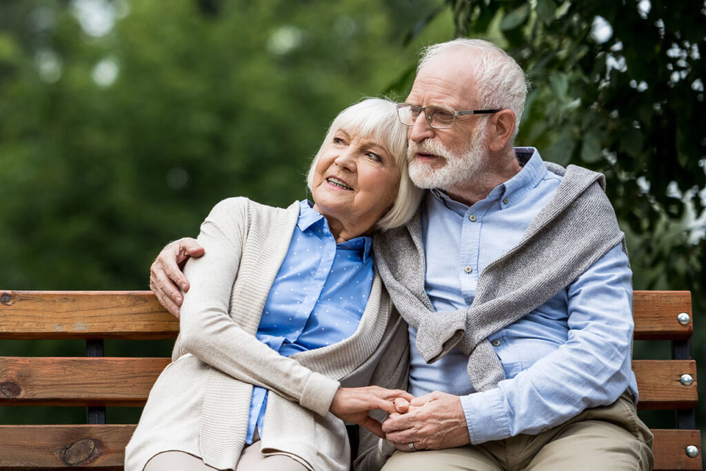 smiling senior couple embracing while sitting on wooden bench in park