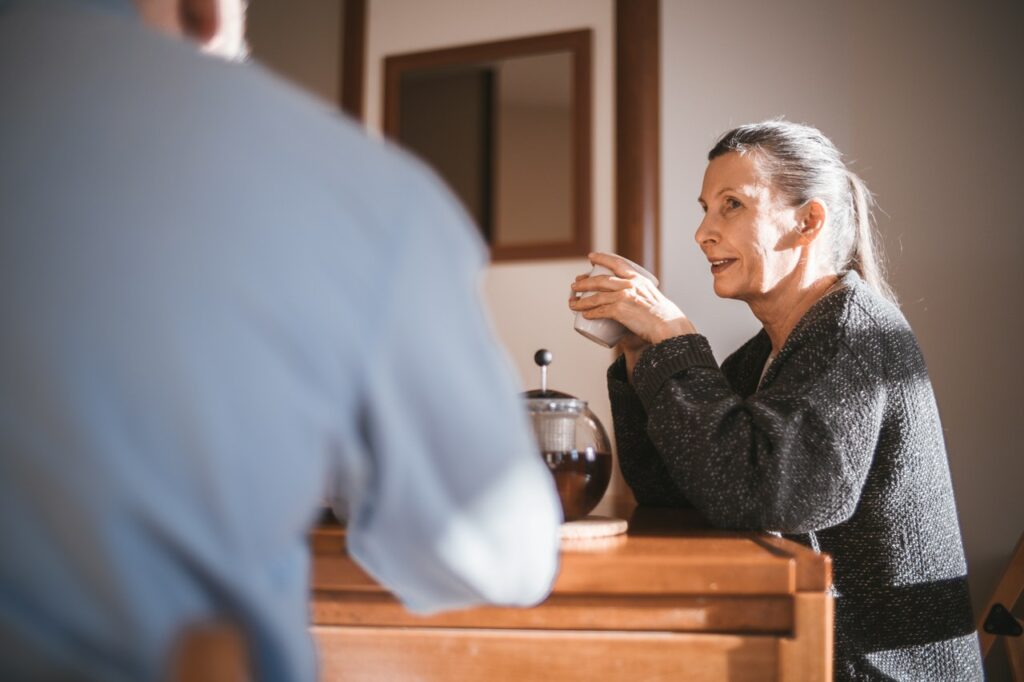Older woman drinking out of a mug looking at someone else