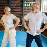 An older man and women stretching before they begin their indoor walking routine.