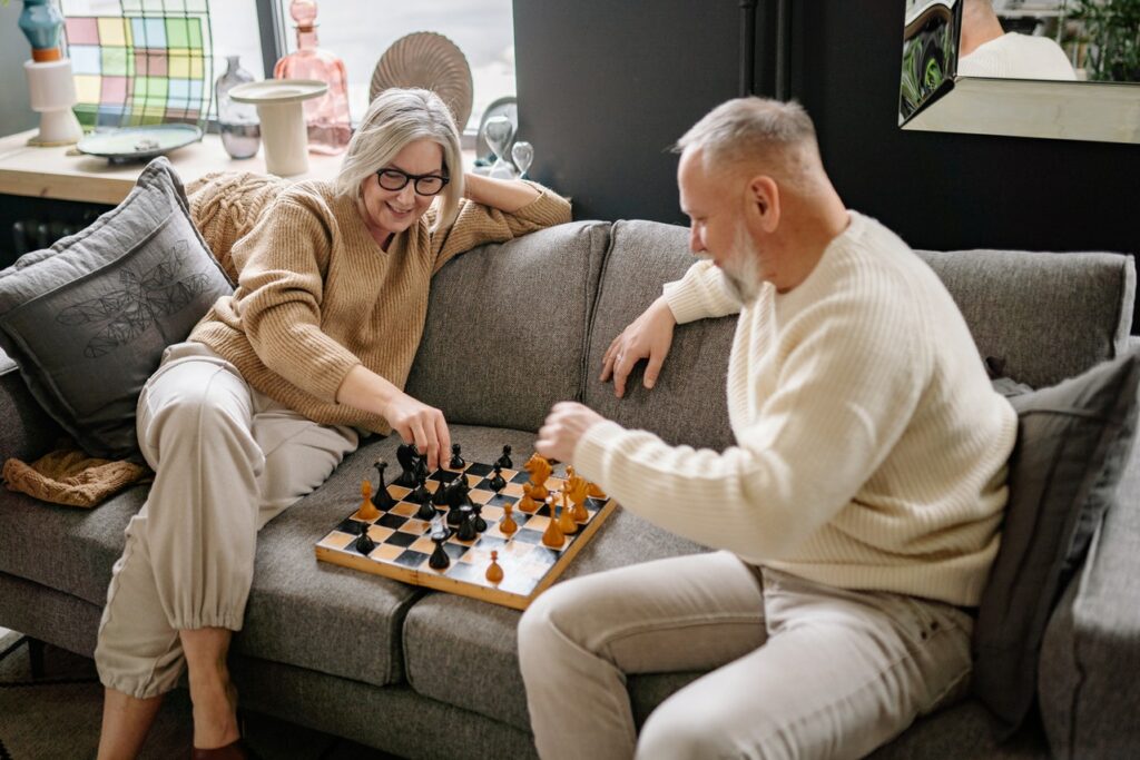 An elderly couple playing chess in their retirement home.