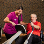 Sweetwater staff member helping resident on fitness bike at onsite wellness center.
