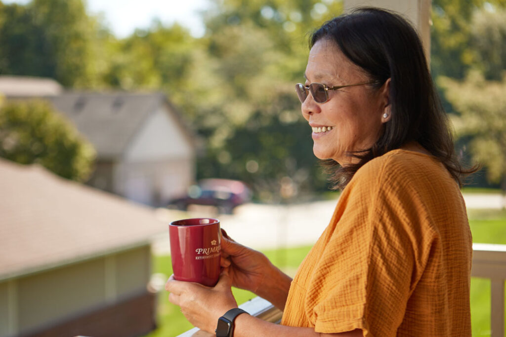 Sweetwater senior female resident looking outside while enjoying a cup of coffee on her patio deck.