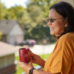 Sweetwater senior female resident looking outside while enjoying a cup of coffee on her patio deck.